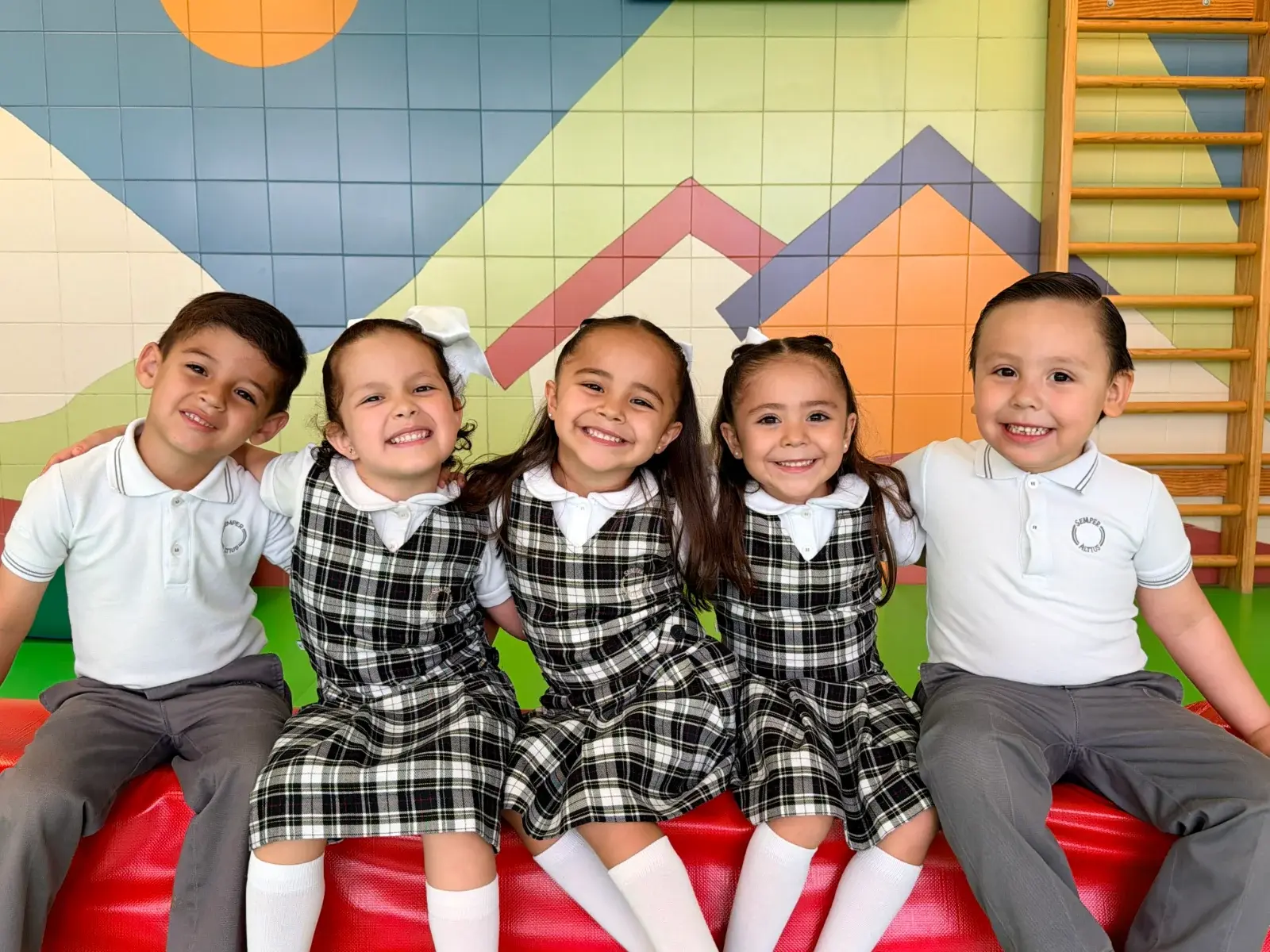 Cinco estudiantes de uniforme escolar sonriendo juntos en el aula durante una actividad grupal
