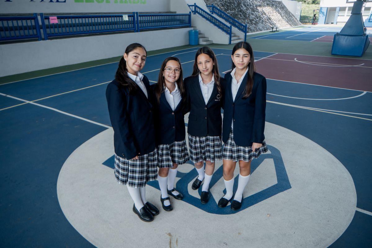 Cuatro estudiantes en uniforme escolar posando en cancha deportiva del colegio